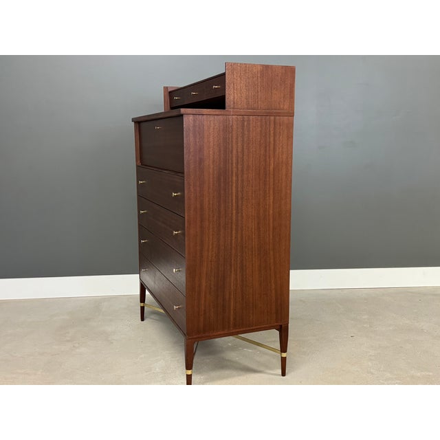 A mid century modern mahogany eleven drawer upright tall gentleman’s dresser with brass knobs and cross stretchers...