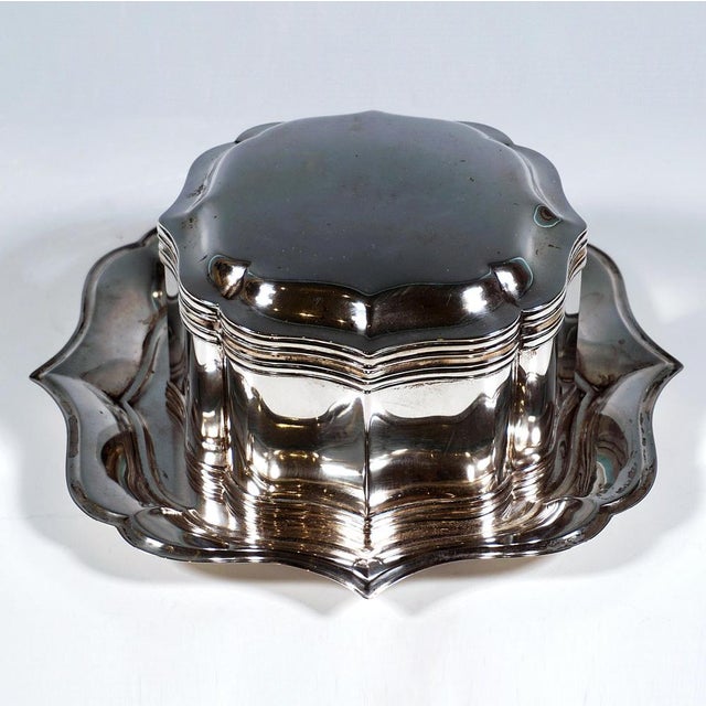 Silver lidded tin on a matching display tray; both items of a curved, elegantly shaped design in the neo-baroque style,...