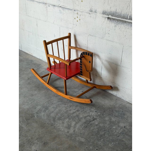 This charming children's rocking horse features a vibrant red seat and a classic spindle backrest. Built with smooth...