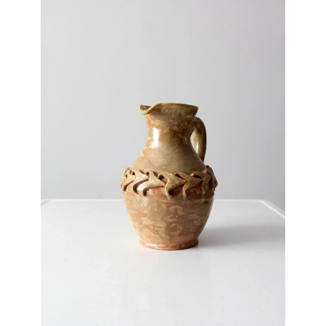A vintage signed studio pottery pitcher, hand-crafted in ceramic with a striking beige and brown glaze. A dynamic chain...