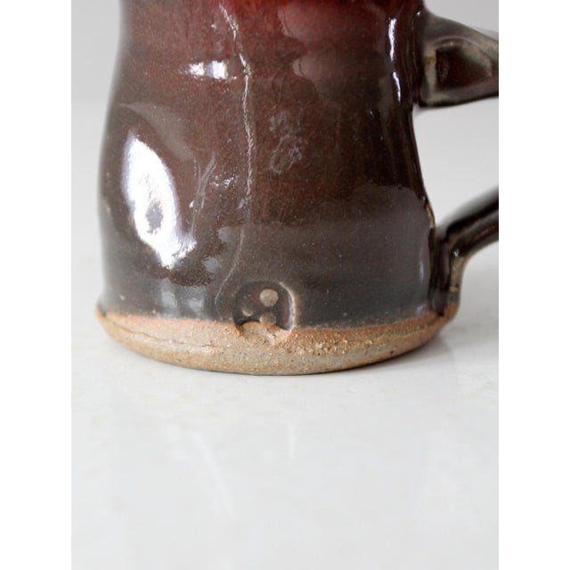 This vintage handmade pottery mug features a slightly barrel-shaped form and a rich, variegated glaze in deep browns and...