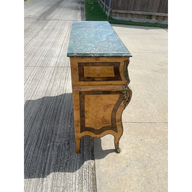 Add timeless European elegance to your home with this breathtaking vintage Regency burlwood commode. Featuring a...