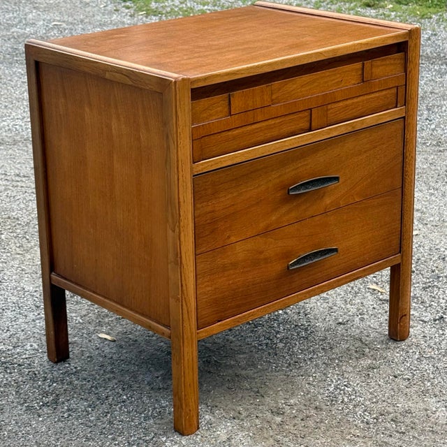 Sleek mid century modern walnut nightstand circa 1960s. Features a brutalist inspired top drawer, one deep drawer for...