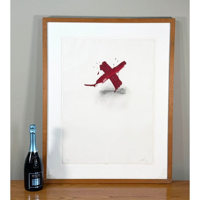 A striking signed limited edition etching by renowned Catalan artist Antoni Tàpies, featuring his iconic gestural red “X”...