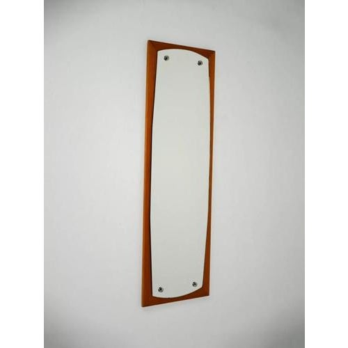 Elegant wall mirror with a rectangular solid teak frame and a shaped internal mirror, secured with metal spacers. A...