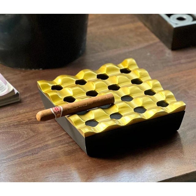 A striking large-format cigar ashtray combining a deep black base with a sculptural brass-tone gold upper section. The...
