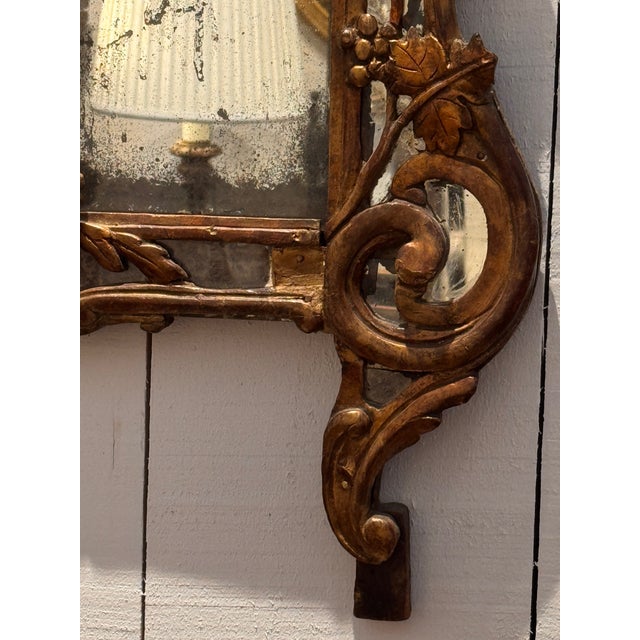 An Italian mirror with a tall rectangular glass framed by elaborate carved scrollwork and vine decoration. Grapes and...