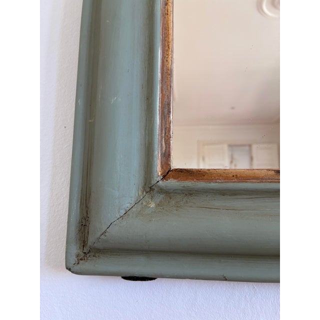 The mirror features a green-painted wooden frame with a gilt edge and a gently curved top characteristic of the Louis...