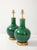 A pair of ceramic table lamps finished in a deep, high-gloss emerald glaze. Each lamp sits on a hand-gilded wood base and...