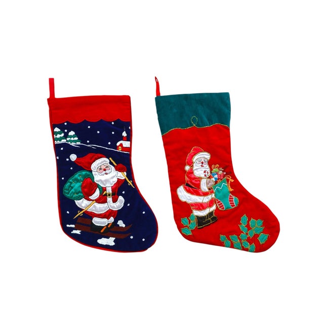 A set of two traditional quilted and embroidered Christmas stockings. Each stocking shows Santa dressed in red. On one he...