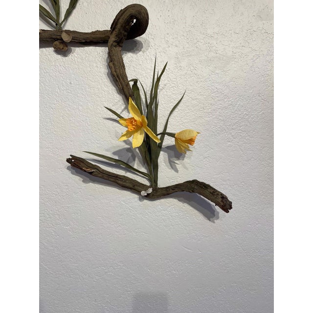 Catch My Drift I features a delicate arrangement of mixed media, combining organic forms with vibrant yellow daffodils....