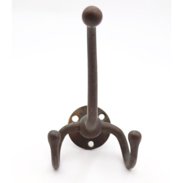 Vintage wall hook made of brass with a very dark finish. The hook features a circular back plate and an elongated arm for...