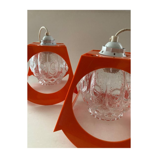 Pair of orange plastic pendant lights with glass globes, in the style of Richard Essig's pendant lights, 1970s. Up to 250V...