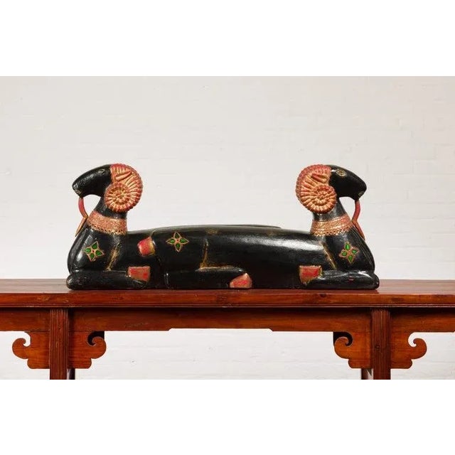 A vintage Northern Thai double ram black painted sculpture from the mid-20th century, with elegant antlers, green glass...