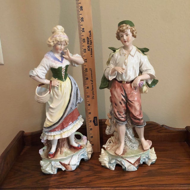 Beautiful antique German porcelain figurines, featuring a young woman with a basket and a young man holding flowers. Both...