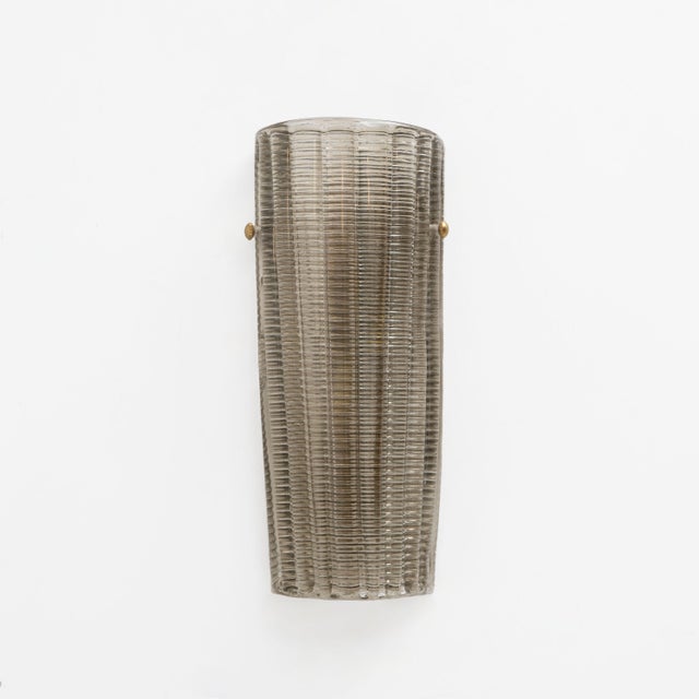 An elegant pair of italian wall lamps featuring hand-crafted murano glass shades in a "fumé" (smoked) tone. The elongated...
