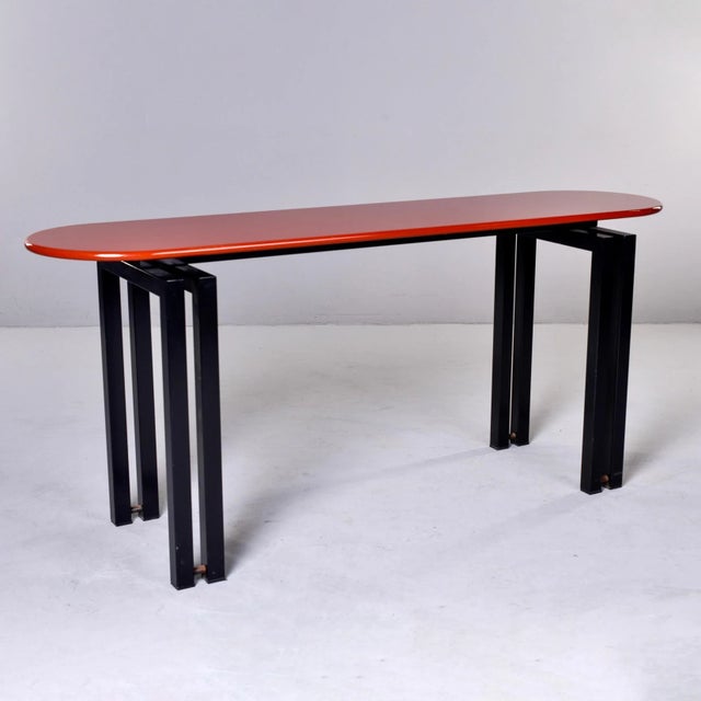 Circa 1980s console by Cidue of Italy features an oval table top with a cinnabar color lacquered top and contrasting base...