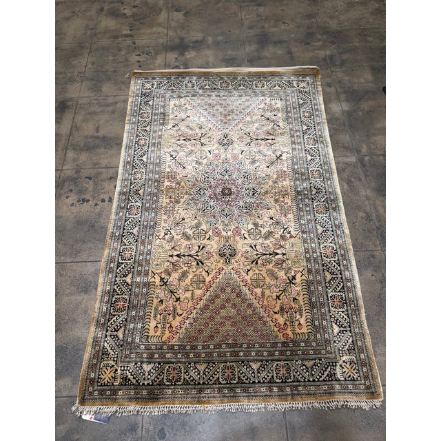 This finely woven silk Qom rug displays a rich and dynamic color palette of gold, black, olive, and subtle red accents,...