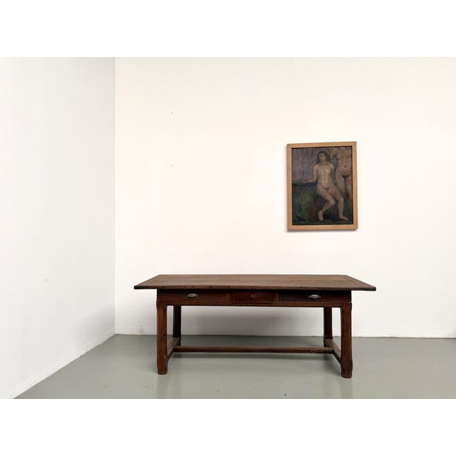 A solid oak farmhouse table from the early 20th century. It features two pull-out drawers and a central drawer. Two shell...