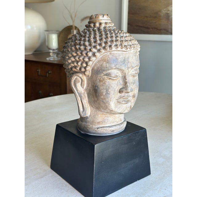 Bring a sense of calm and sculptural presence to your space with this antiqued Buddha head sculpture, beautifully rendered...