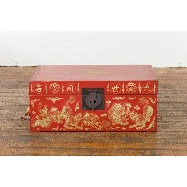 A small Chinese red lacquered wedding blanket chest from the 20th century, with gilt décor depicting guardian lions,...