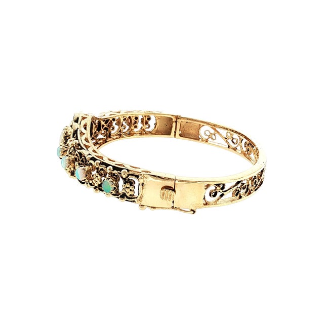 A mid-century Victorian revival 14k gold hinged bracelet with opal cabochons. This piece features intricate filigree work...