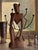 Striking hand-carved wood sculpture from Ghana depicting a stylized seated figure in a contemplative pose. The elongated...