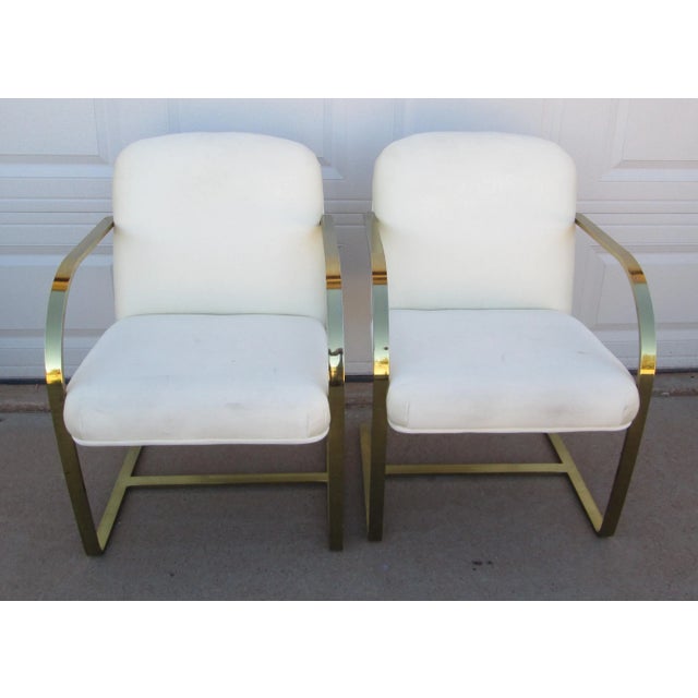 2 Brno style chairs (designed by Ludwig Mies van der Rohe) with flat arm gold tone metal and light fabric. The chairs are...