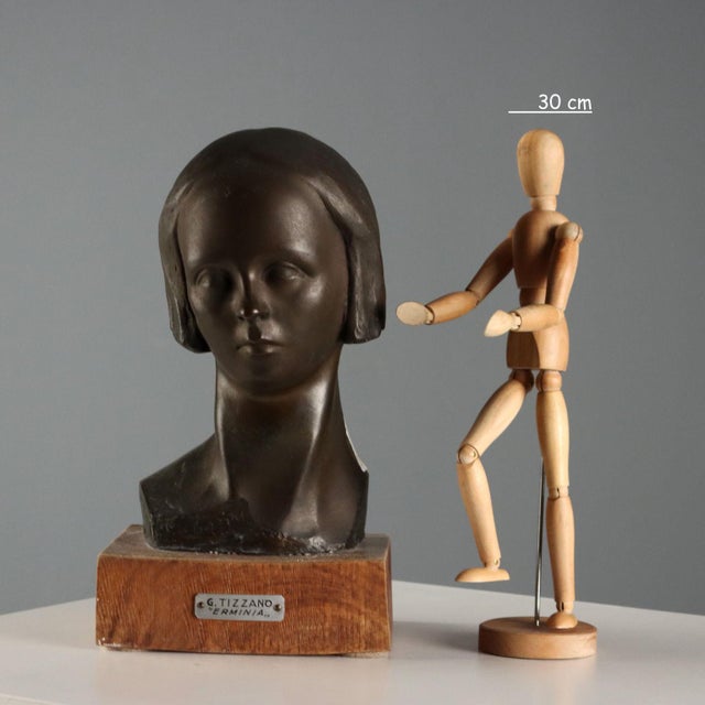 Bronze sculpture on a wooden base depicting a girl's head, titled 'Erminia'. Engraved signature. This piece is attributed...