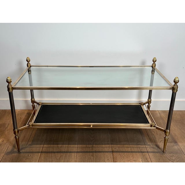 This beautiful neoclassical-style coffee table is made of brass with a clear glass top and a black leather lower tray. It...
