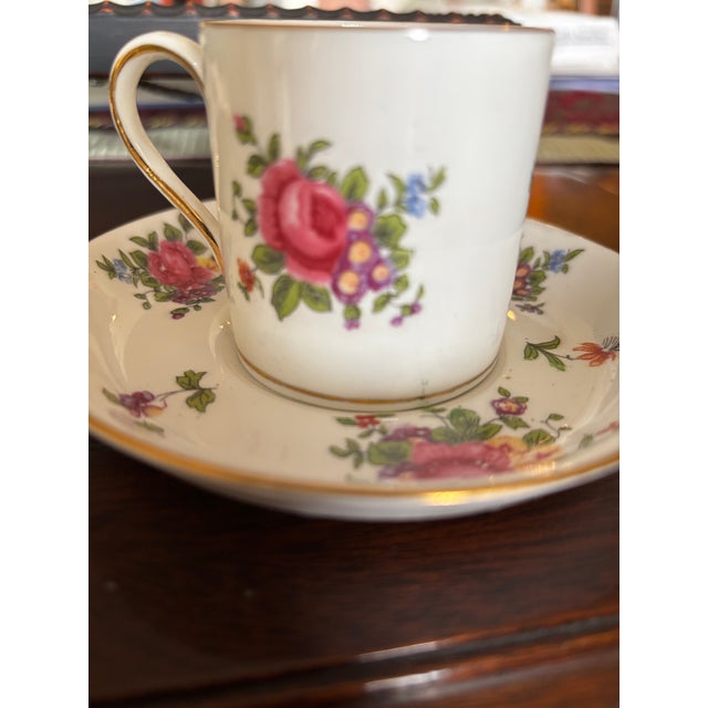 Made in England, this elegant demitasse cup and saucer features a classic white background beautifully adorned with a...