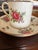 Made in England, this elegant demitasse cup and saucer features a classic white background beautifully adorned with a...