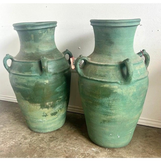 Pair of large ceramic urns, each with a robust, rounded body and a narrow, flared neck. The urns are finished in a...