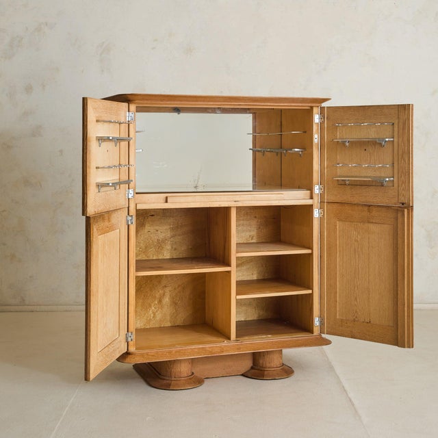 A 1940s French oak bar cabinet, defined by its paneled facade and parquetry veneer. The façade is defined by four doors,...