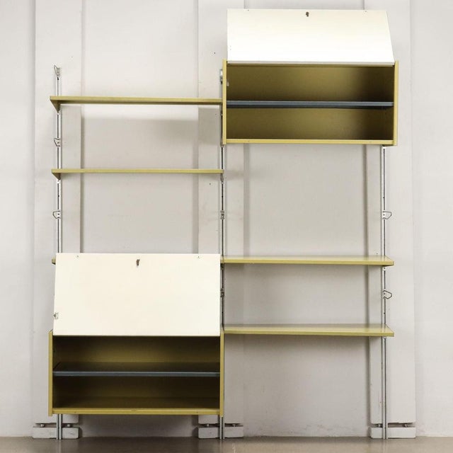 Wall-mounted bookcase requiring wall anchoring, with open shelves and storage elements, uprights made of aluminium and...