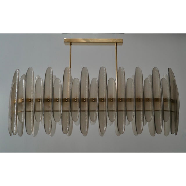 Murano chandelier with an elongated design, featuring a brass frame and single smoked glass. The glass half-shell is...