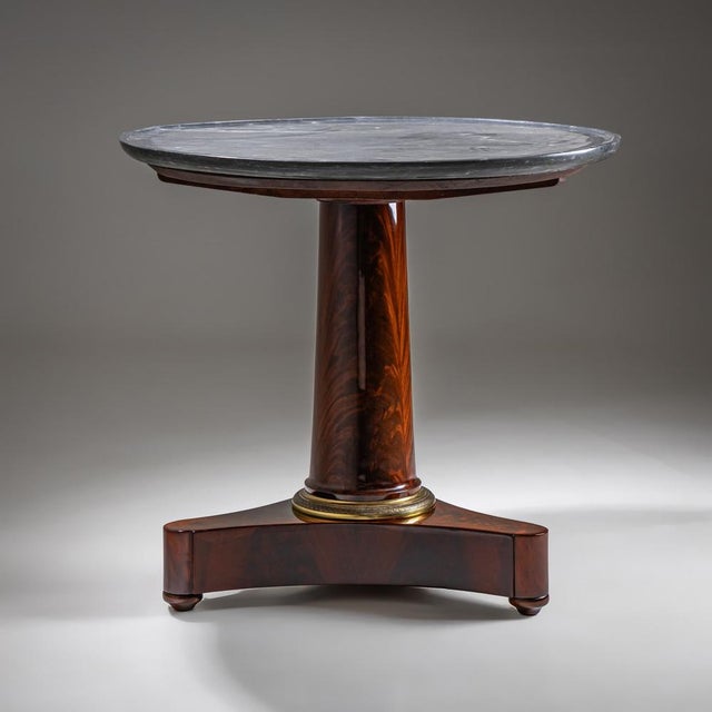 Round side table dating to around 1830, featuring a dark grey marble top. The base is made of mahogany veneer with a...