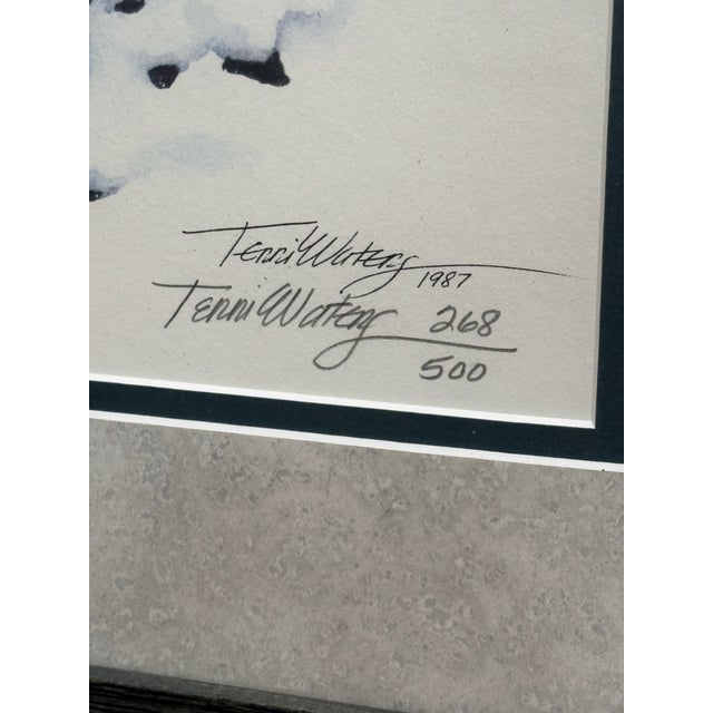 Charming winter landscape print by Terri Waters, dated 1987, depicting a snow-covered cabin nestled among trees in a...