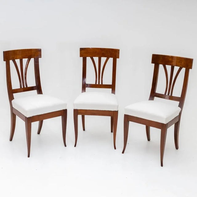 Set of three Biedermeier chairs in walnut with white upholstered seats and backs with three struts. The chairs stand on...