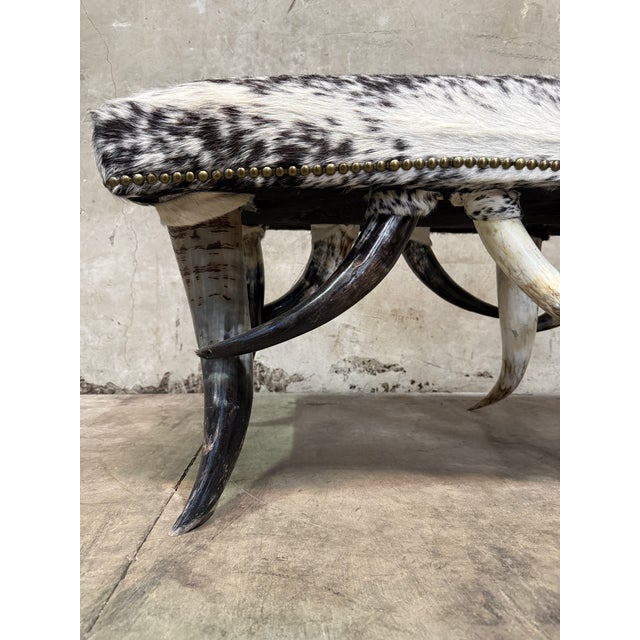 A bold steer horn bench with a speckled cowhide seat — real presence and real materials. The base is built entirely from...