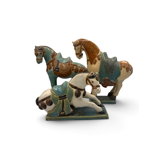 A decorative set of three Chinese-style ceramic horse figures inspired by Tang dynasty forms. Each horse is individually...