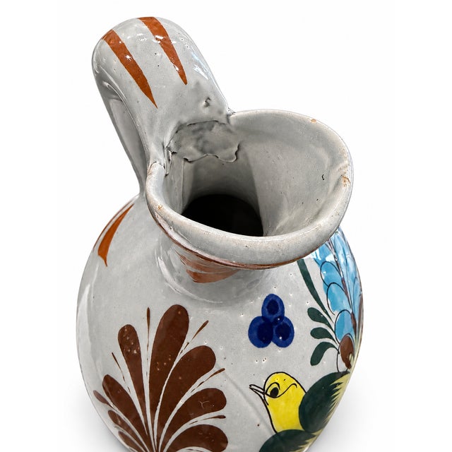 Charming vintage handcrafted ceramic pitcher featuring a light gray glazed body decorated with vibrant, hand-painted blue...