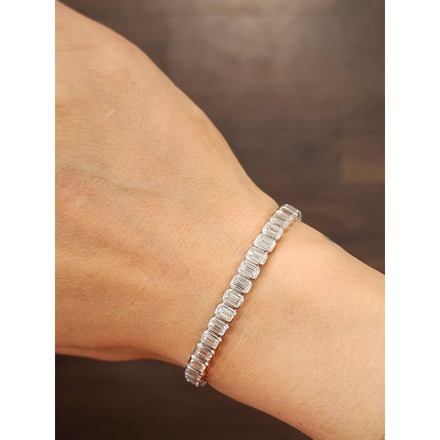 A modern platinum tennis bracelet featuring 44 natural emerald-cut white diamonds totaling 8.64 carats, graded G/H color...