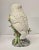 Beautiful white ceramic owl perched on a tree branch.The eyes are striking, so intense.The bird is looking around, almost...