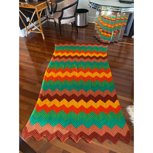 A vintage mid-century throw blanket, hand crocheted in a chevron zigzag pattern featuring bright contrasting colors of...