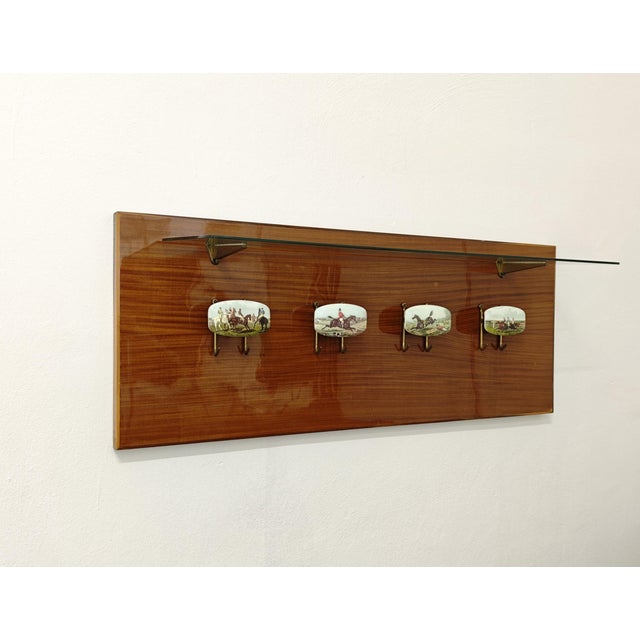 Wooden wall-mounted coat rack with a glass shelf supported by two brass supports with a mechanism. Decorative knobs and...