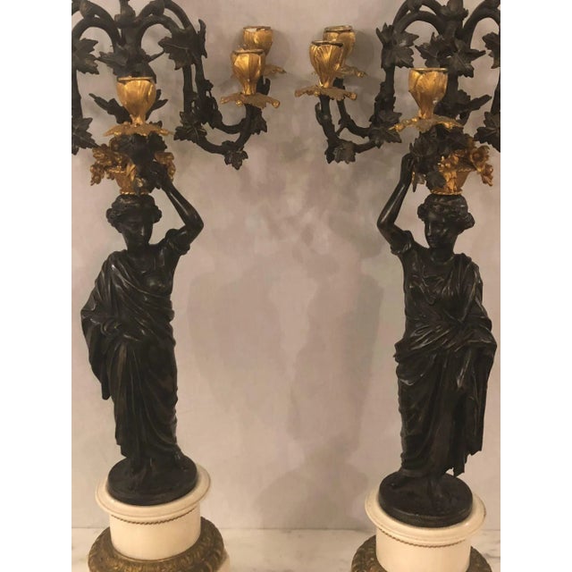 Pair of neoclassical style bronze six-arm figural candelabra. Each depicting a maiden in Greek garments serving a basket...