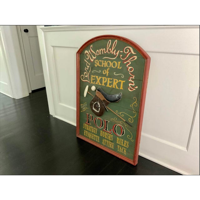 An arched wooden sign painted in olive green with a burgundy border, advertising "Lord Wembly-Thorn's School of Expert...