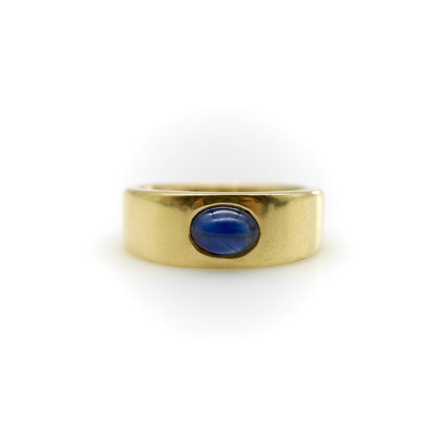 Circa the 1970’s, this 18k gold vintage Tiffany & Co. ring is a simple, wide cigar band with a central natural blue...