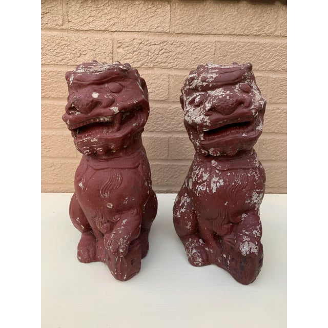 A wonderfully weathered pair of antique cast stone foo dogs, retaining their original red painted finish with beautifully...